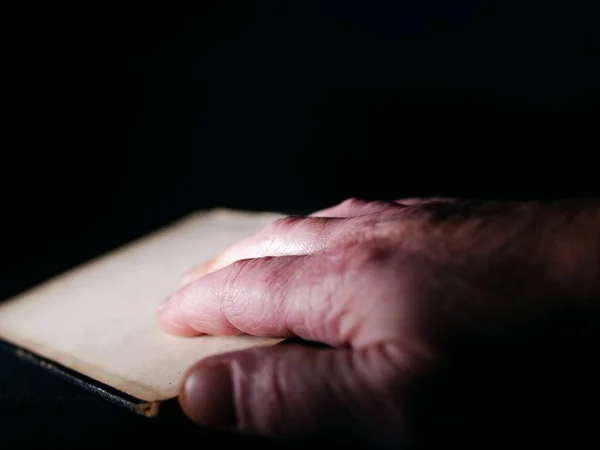어둠의 배경에 관한 책을 읽고 있는 노인의 손 — 스톡 사진