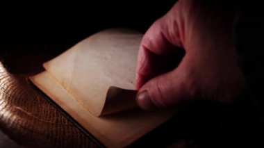 Hand opens old worn book on dark background