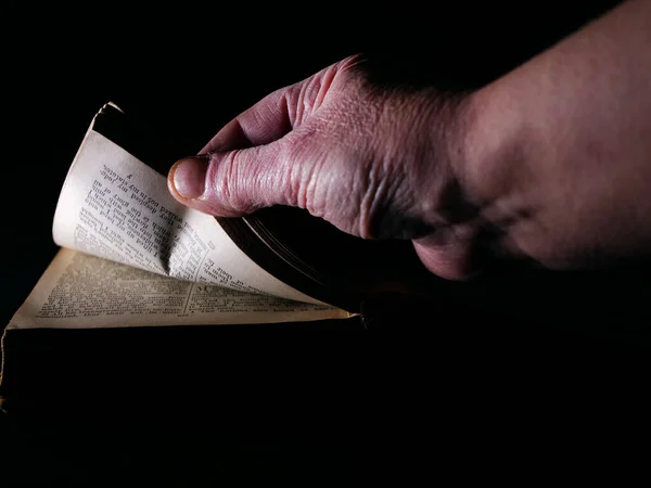 Páginas de abertura de mão de uma Bíblia antiga no fundo escuro — Fotografia de Stock