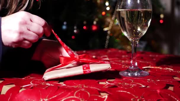 Hands unwrapping Christmas gift with glass of white wine — Stok Video