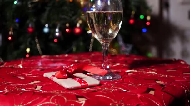 Ποτήρι λευκό κρασί με δώρο τα Χριστούγεννα bokeh φώτα φόντο — Αρχείο Βίντεο
