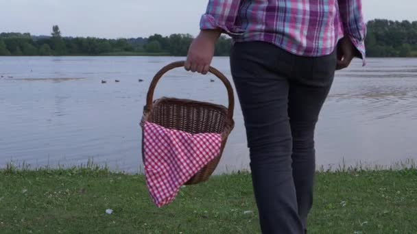 Woman stands by lake shore with vintage picnic basket — Stock Video