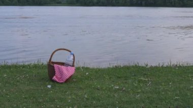Göl kenarında kırmızı pamuklu kumaşlı piknik sepeti. 