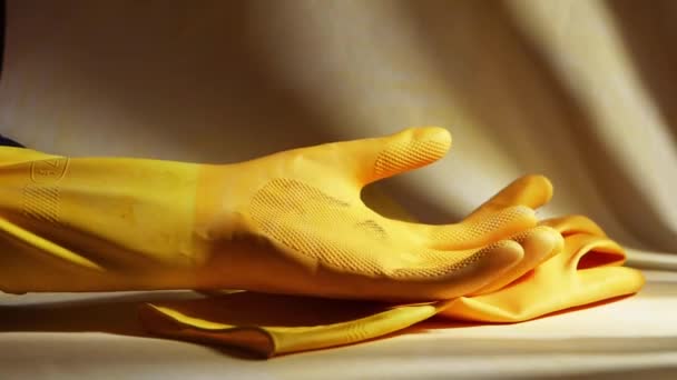 Hand puts on yellow rubber cleaning gloves on a yellow background — Stock Video