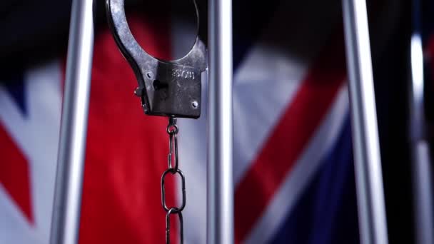 Handcuffs swing on prison bars with Union jack British flag background — Stock Video