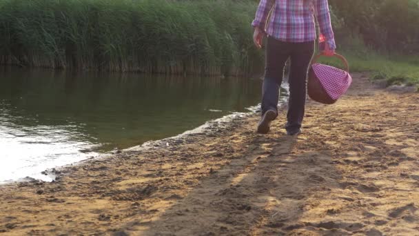 Orilla del lago con la mujer en el fondo con la cesta de picnic vintage — Vídeo de stock