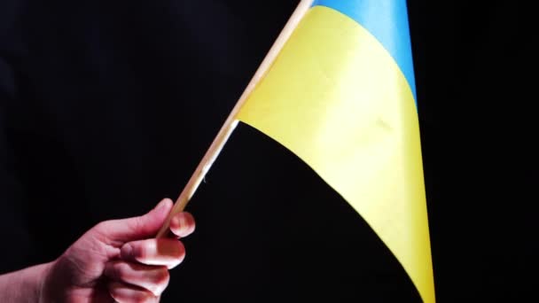 Ręka trzyma Ukrainę żółto-niebieską flagę na czarnym tle — Wideo stockowe