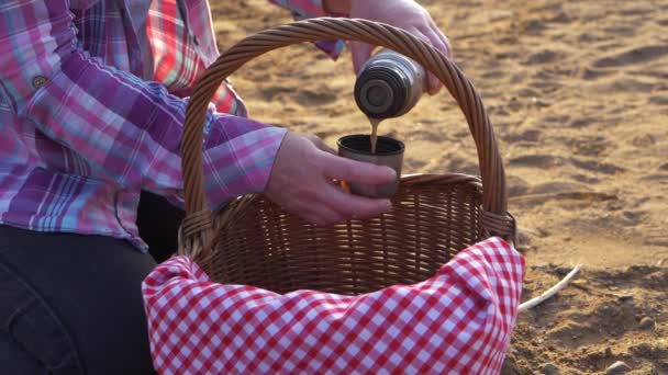 Mujer con cesta de picnic vierte café del termo en el lado del lago — Vídeo de stock