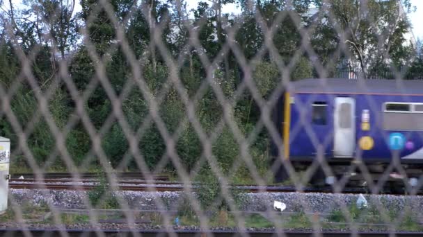 Zug nähert sich Bahnhofsblick durch Zaun — Stockvideo