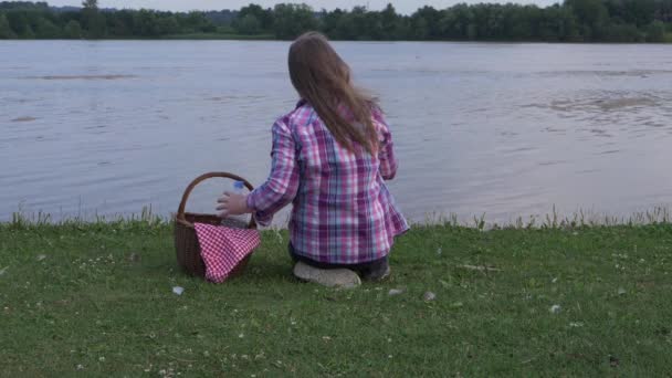 Mujer con cesta de picnic mira hacia el lago — Vídeo de stock