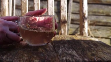 Kırsal arka planda papatya çayı bardağı tutan eller.