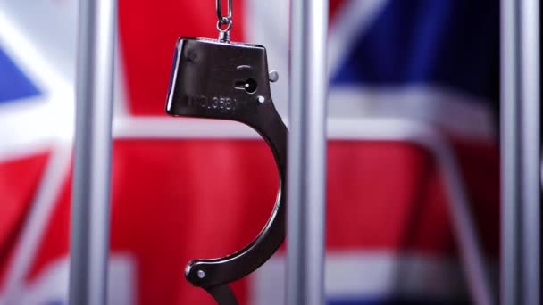 Las esposas oscilan en las barras de la prisión con el fondo de bandera británica Union jack — Vídeo de stock