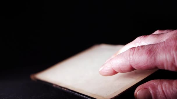 Mano de anciano leyendo un libro sobre fondo oscuro — Vídeos de Stock