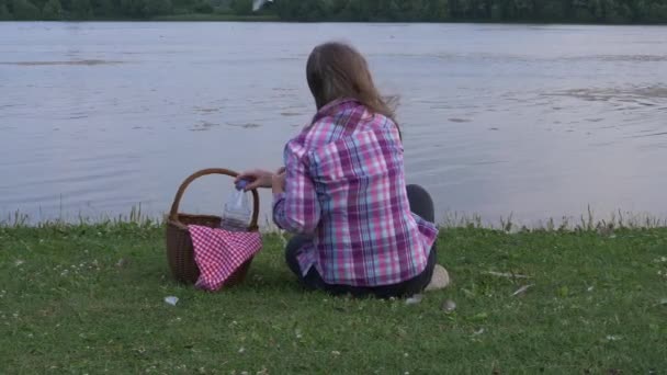 Vrouw met picknickmand kijkt uit op meer — Stockvideo