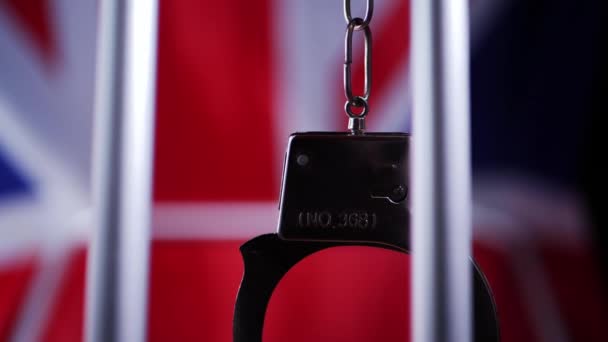 Handcuffs swing on prison bars with Union jack British flag background — Stock Video