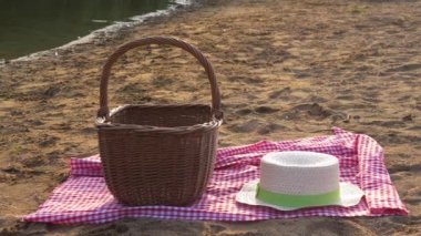 Picnic basket with red gingham cloth and straw hat on the beach sand 