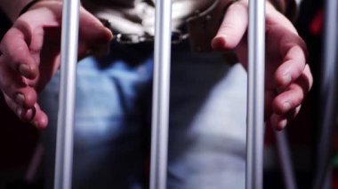 Kelepçeli mahkum parmaklıklardan uzanıyor. Orta yavaş çekim seçici odak noktası.
