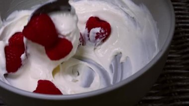 Orta boy bir kasede ahududu ve kremalı Yunan yoğurdu karıştırmak 4K seçici odak noktası