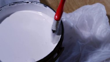 Evi dekore etmek için boya fırçasını beyaz boyaya batırıyorum. Yavaş çekim 4k seçici odak noktası.