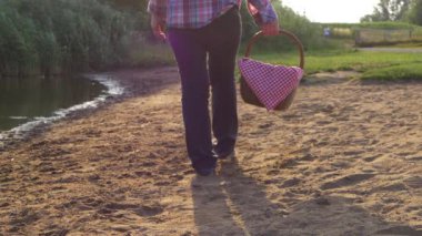 Kadın klasik piknik sepetiyle göl kıyısında yürüyor. Yavaş çekim, seçici odak noktası.