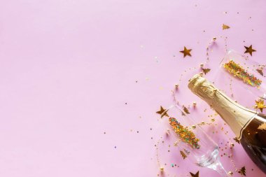 Bir şişe şampanya ve üzerine pembe arka planda konfeti serpiştirilmiş bardaklar. Mutlu noeller için yeni yıl mesajları.