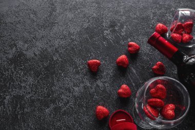 Şarap, kalpli şarap kadehleri ve Sevgililer Günü için alyans. Karanlık arka planda mesaj için yer var.