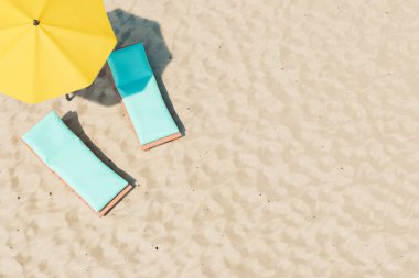 Plajdaki kumlu plajda sarı şemsiyeye yakın yumuşak yastıklı rahat iskemlelerin 3 boyutlu çizimi