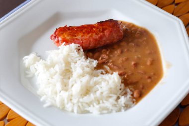 Beyaz tabakta hazır pilav, fasulye ve sosis.