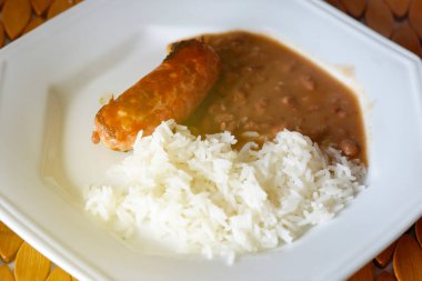 Beyaz tabakta hazır pilav, fasulye ve sosis.