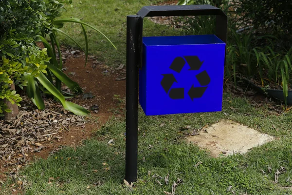blue metal trash can with recycling symbol in green public area and garden - garbage collection