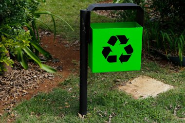 Yeşil halka açık alanda ve bahçede geri dönüşüm sembolü olan yeşil metal çöp kutusu - çöp toplama