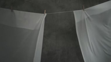 Beyaz kumaş çarşaflar ipteki mandallarla kurutulur. Dalgalı kumaş rüzgarda sallanıyor. Soyut gri arkaplan.