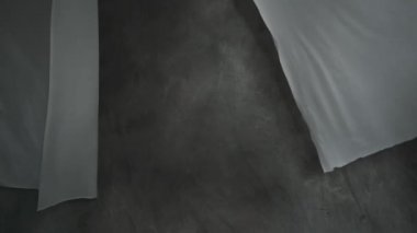 Beyaz kumaş çarşaflar ipteki mandallarla kurutulur. Dalgalı kumaş rüzgarda sallanıyor. Soyut gri arkaplan.