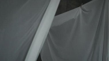 Beyaz kumaş çarşaflar ipteki mandallarla kurutulur. Dalgalı kumaş rüzgarda sallanıyor. Soyut gri arkaplan.