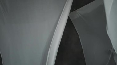 Beyaz kumaş çarşaflar ipteki mandallarla kurutulur. Dalgalı kumaş rüzgarda sallanıyor. Soyut gri arkaplan.