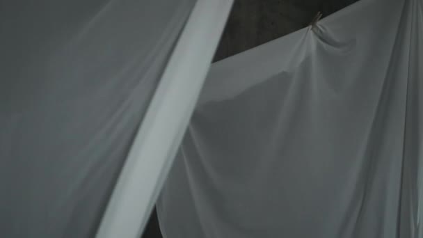 As folhas de tecido brancas secam-se em espinhas de roupa em uma corda. O tecido ondulado oscila ao vento. Fundo cinza abstrato. — Vídeo de Stock