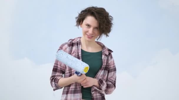 A young adult cheerful woman with blue paint using a roller. Repair and renovation of the design of home room apartment. DIY repair of the house. — 비디오