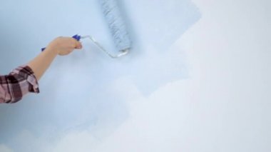 A young adult cheerful woman with blue paint using a roller. Repair and renovation of the design of home room apartment. DIY repair of the house.