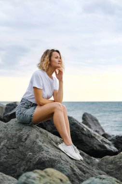 35 yaşında, genç, beyaz, sarışın bir kadın deniz kıyısındaki kayalarda oturuyor. Zümrüt renkli su, taşlara vuran dalgalar. Kadın meditasyon yapıyor ve rahatlıyor..