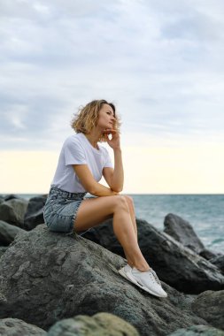 35 yaşında, genç, beyaz, sarışın bir kadın deniz kıyısındaki kayalarda oturuyor. Zümrüt renkli su, taşlara vuran dalgalar. Kadın meditasyon yapıyor ve rahatlıyor..