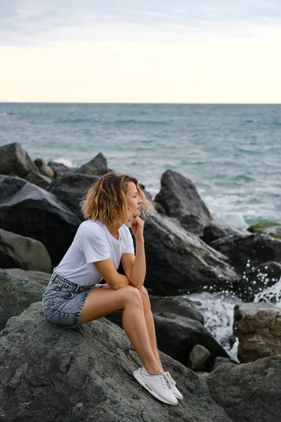 35 yaşında, genç, beyaz, sarışın bir kadın deniz kıyısındaki kayalarda oturuyor. Zümrüt renkli su, taşlara vuran dalgalar. Kadın meditasyon yapıyor ve rahatlıyor..