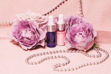 Gümüş boncuklu parlak pembe kumaş arka planda cam şişeler. Gül özlü serum ya da aroma yağı