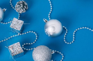 Mavi arka planda altın ışıkları olan gümüş Noel süslemeleri. Noel baloları, hediye kutuları, kozalaklar ve ağaç için yeni yıl boncukları. Düz yatıyordu.