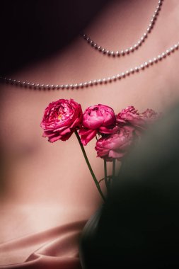 Bir demet gül ve parlak pembe kumaş arka planında bir vazo ile sakin bir hayat. Tekstil gümüş boncuklarla süslenmiş. Uzayı kopyala, dikey