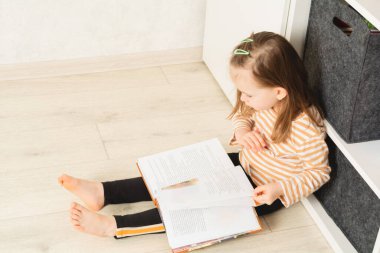 Yerde oturan ve evde kitap okuyan sevimli bir bebek. Evde boş vakit ve eğitim. Boşluğu kopyala