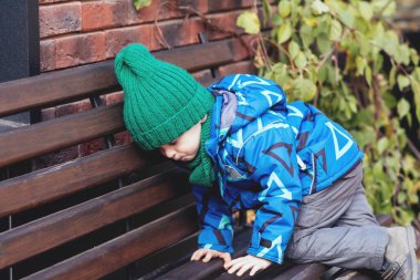 Parktaki küçük bir çocuk bir bankın üzerine tırmanır. Mutlu aile ve çocukluk kavramı. Dışarıda sağlıklı bir bebek
