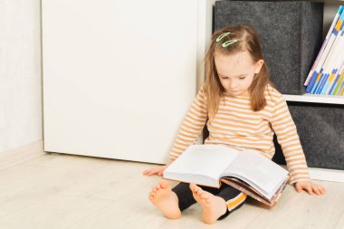 Yerde oturup kitap okuyan sevimli bir bebek.