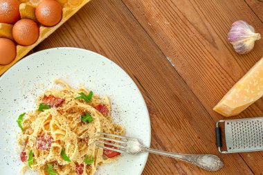 Domuz pastırmalı ve parmesanlı ev yapımı İtalyan makarna. Yumurta, sarımsak, rende ve peynir. Geleneksel İtalyan mutfağı. Ahşap arka plan. Üst Manzara. Boşluğu kopyala