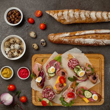 Koyu arkaplanda sandviçler, çeşitli kanepeler, pintxolar, tapalar. Sosisli, jambonlu, salamlı, pastırmalı, baget, peynirli, domatesli, zeytinli, yumurtalı, ayyaş ve otlu sandviç. Anlaşıldı.