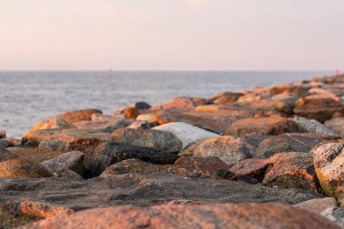 Gün batımında sahilde kayalar. Güneş, kaya iskelesinin üzerinde batıyor. Sakin bir akşamda, pembe günbatımında deniz kıyısında dalgalanan sular.